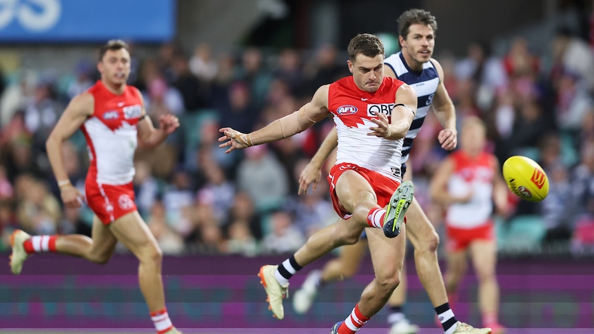 A Sydney Swans player kicks around his body towards goal during a game.