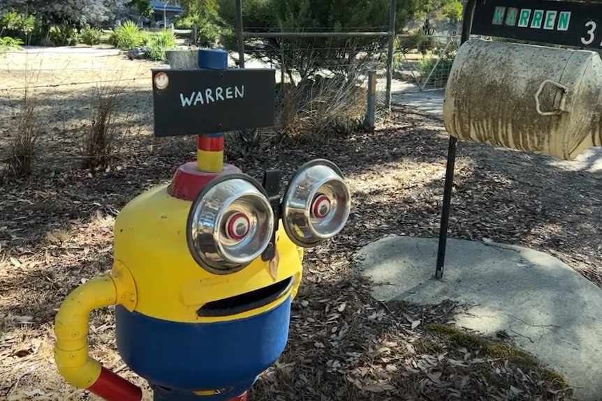 A minion with dog bowls for eyes rests next to a more conventional mailbox. Both have the word "Warren" on them