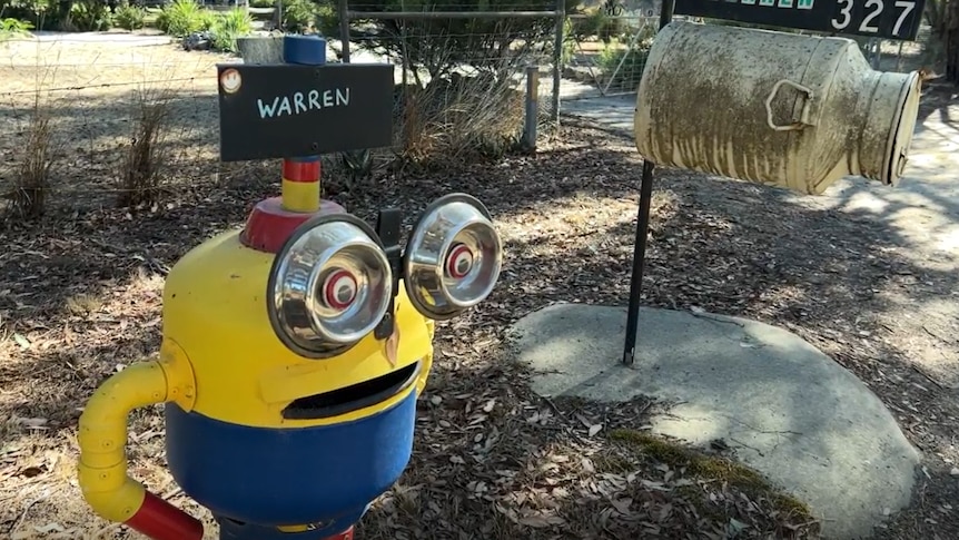 A minion with dog bowls for eyes rests next to a more conventional mailbox. Both have the word "Warren" on them