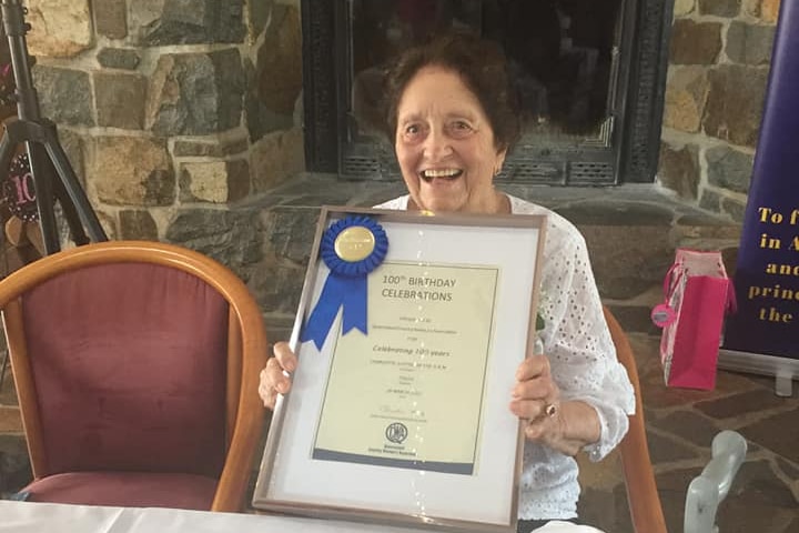 Lottie Hastie holding a framed certificate and a ribbon for her 100th birthday