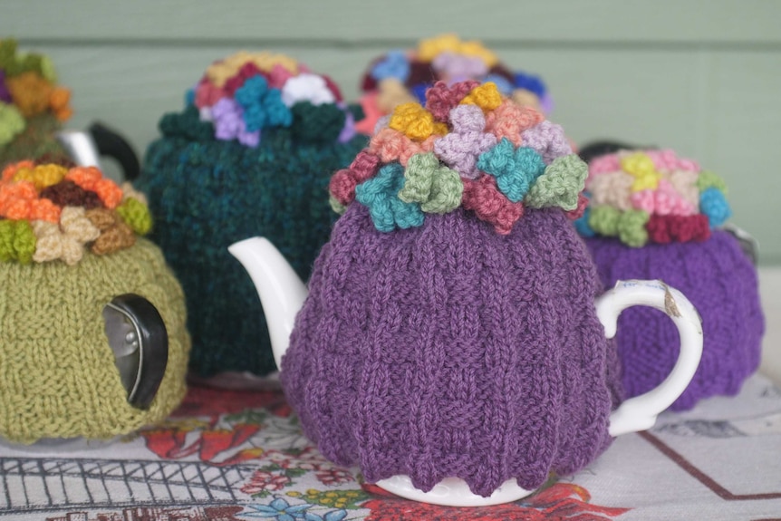 A collection of tea pots on a table, with colourful knitted tea cosies sitting on them.