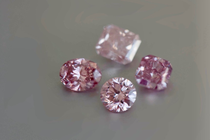 Four pink coloured diamonds and a pair of tweezers.