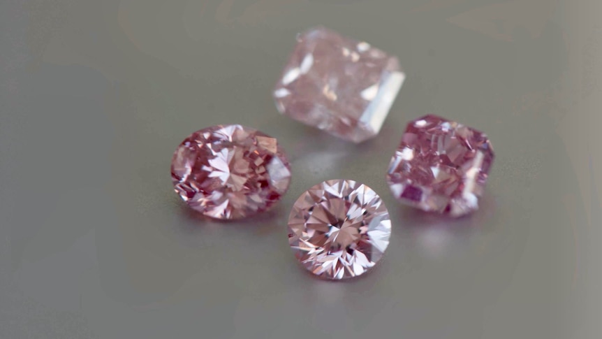 Four pink coloured diamonds and a pair of tweezers.