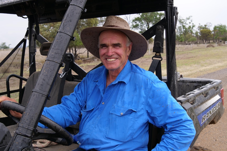 A farmer sits in a four wheeler buggy in a blue work shirt and hat