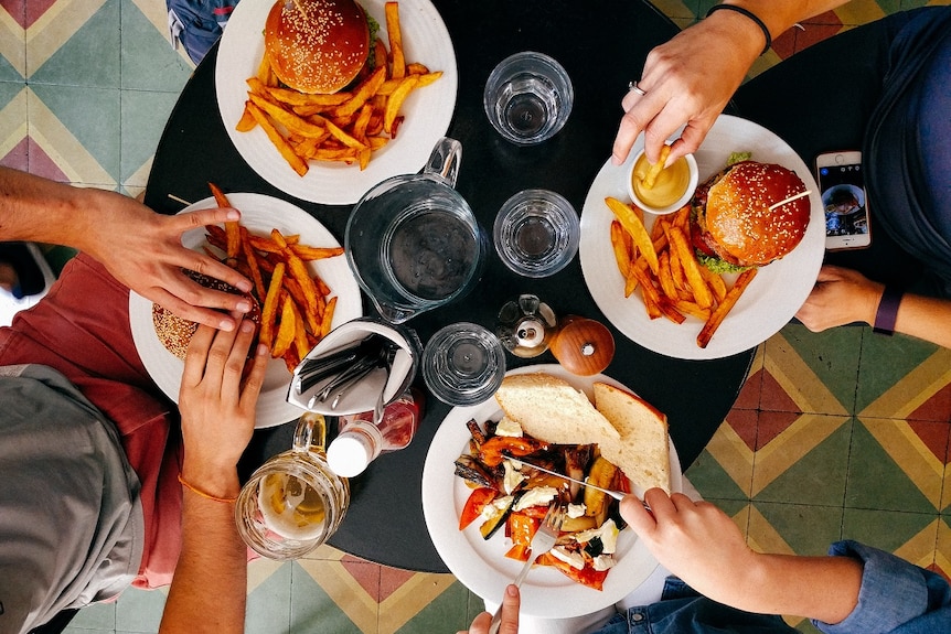 Overhead view of a table with burgers and chips with four people sitting around it.