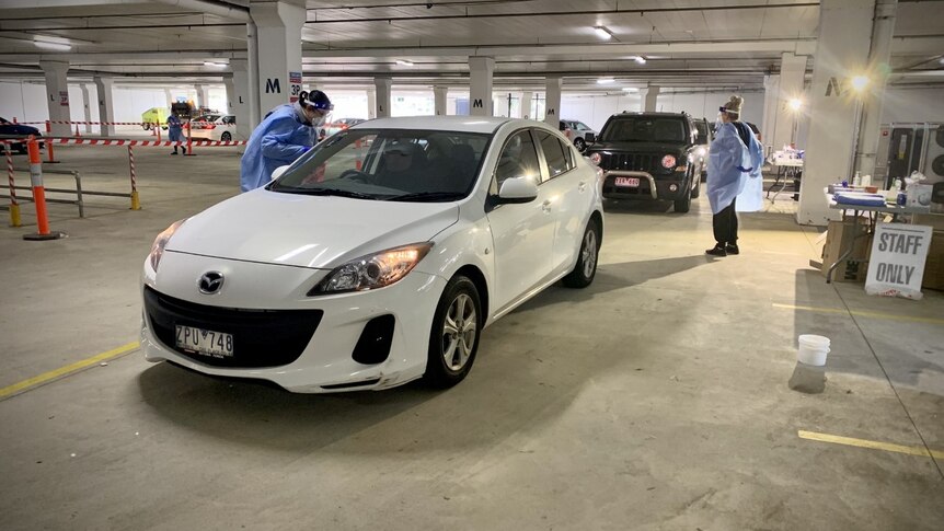 Cars line up in an underground carpark and are approached by health workers for a coronavirus test.
