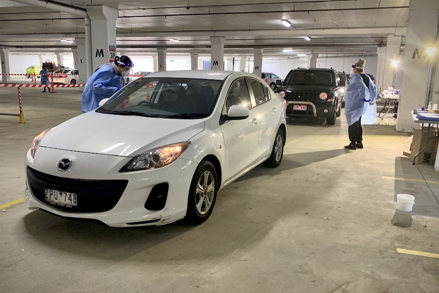 Cars line up in an underground carpark and are approached by health workers for a coronavirus test.