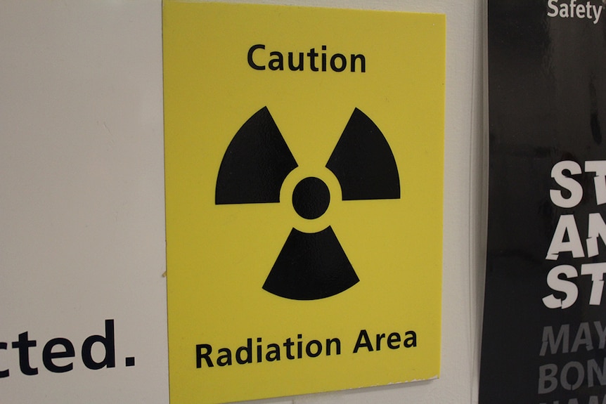 Yellow "Caution, Radiation Area" sign stuck to a white wall.