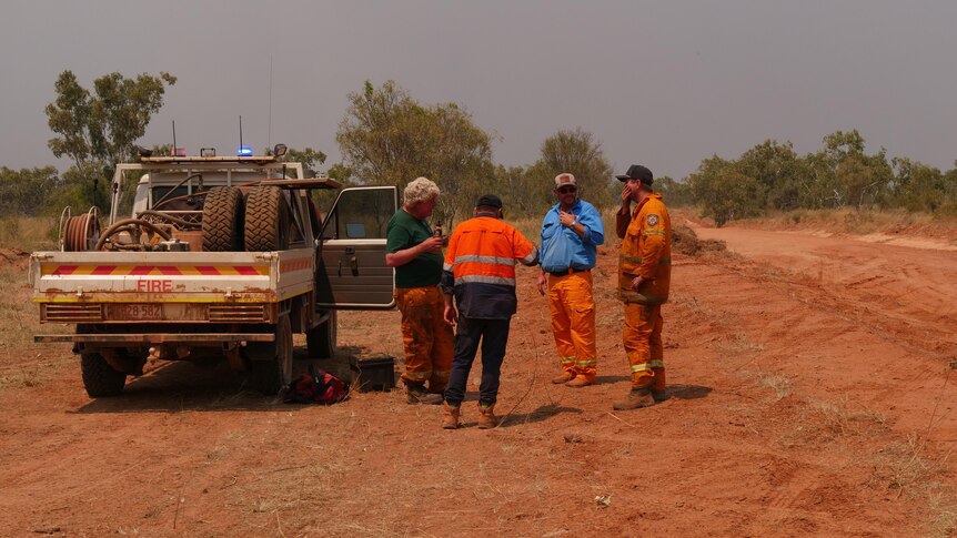 Four men in high vis stand next to a truck in smoky conditions