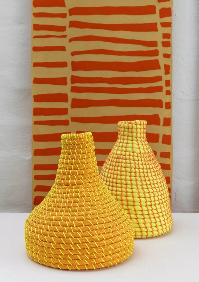 Uma obra de arte têxtil; dois vasos cônicos tecidos em laranja e amarelo brilhantes.