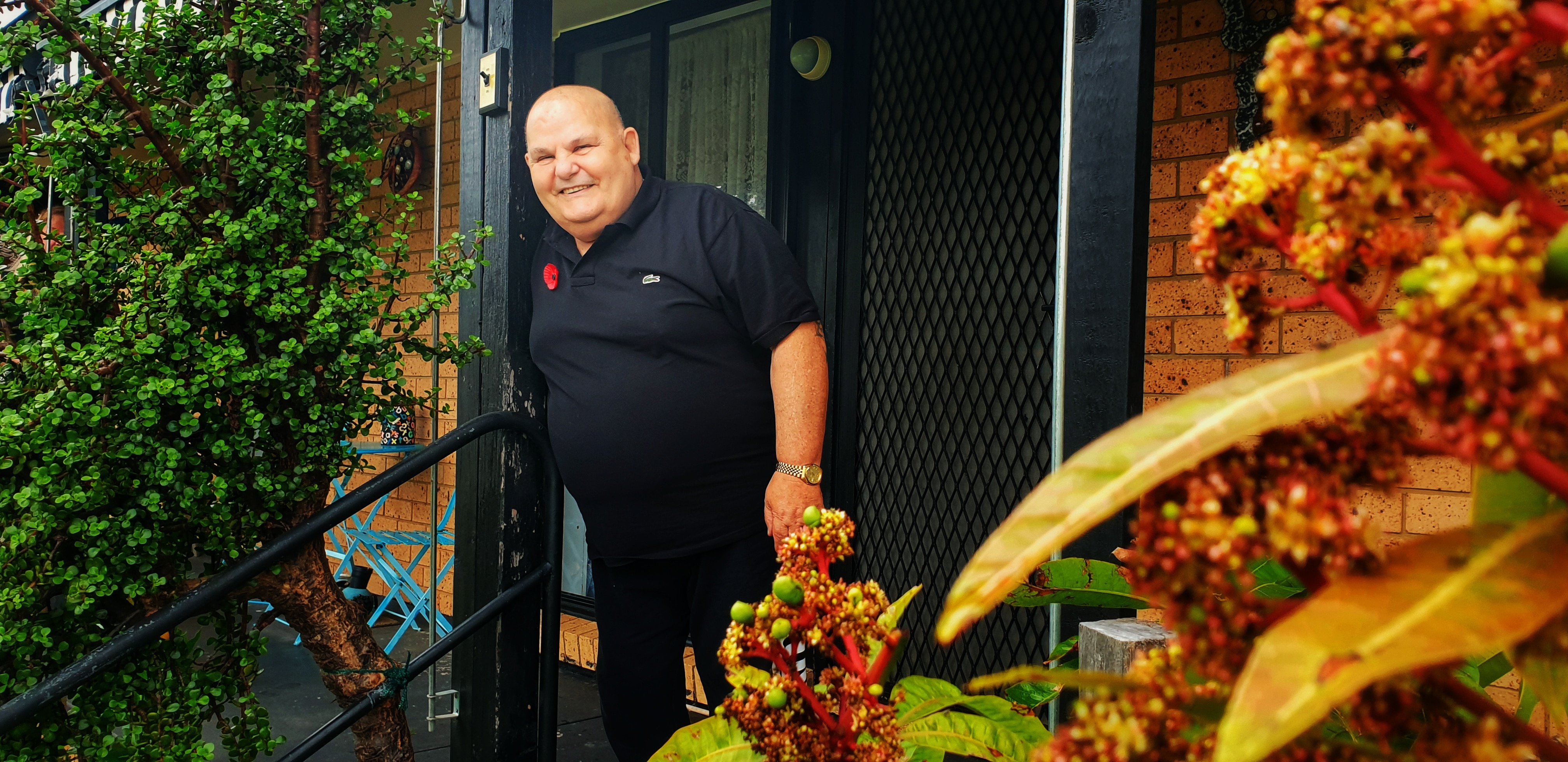 A man wearing a black shirt standing on a front porch smiling.