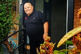 A man wearing a black shirt standing on a front porch smiling.