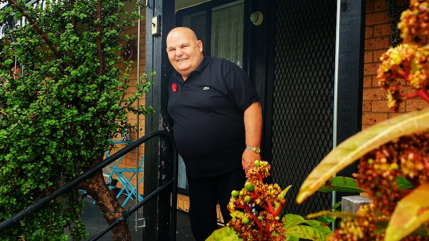 A man wearing a black shirt standing on a front porch smiling.