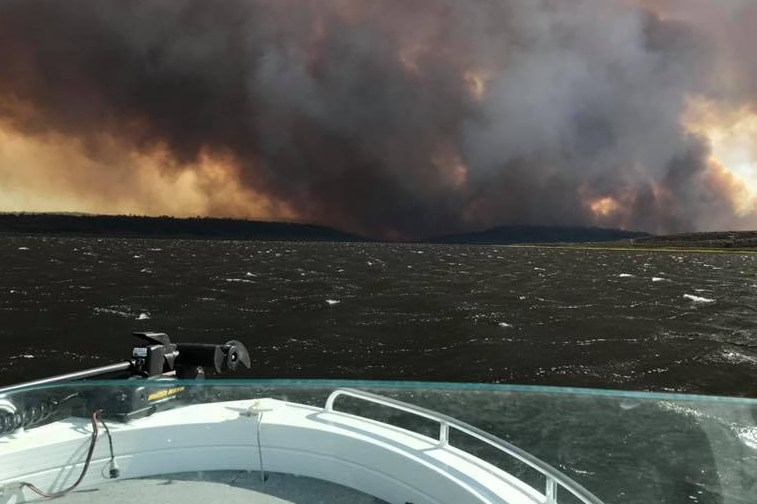 Photo taken from boat on lake showing smoke from bushfire on shore.