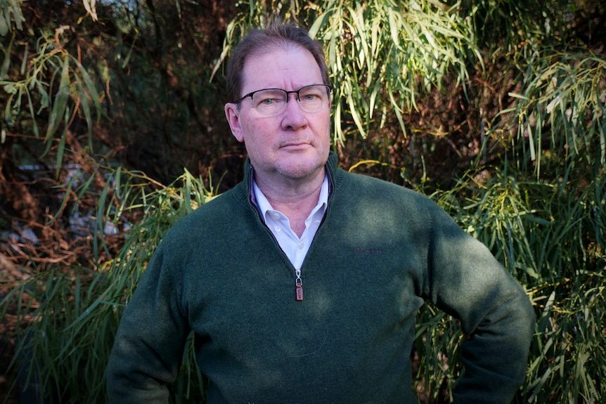 a man in glasses and a green jumper looks at the camera
