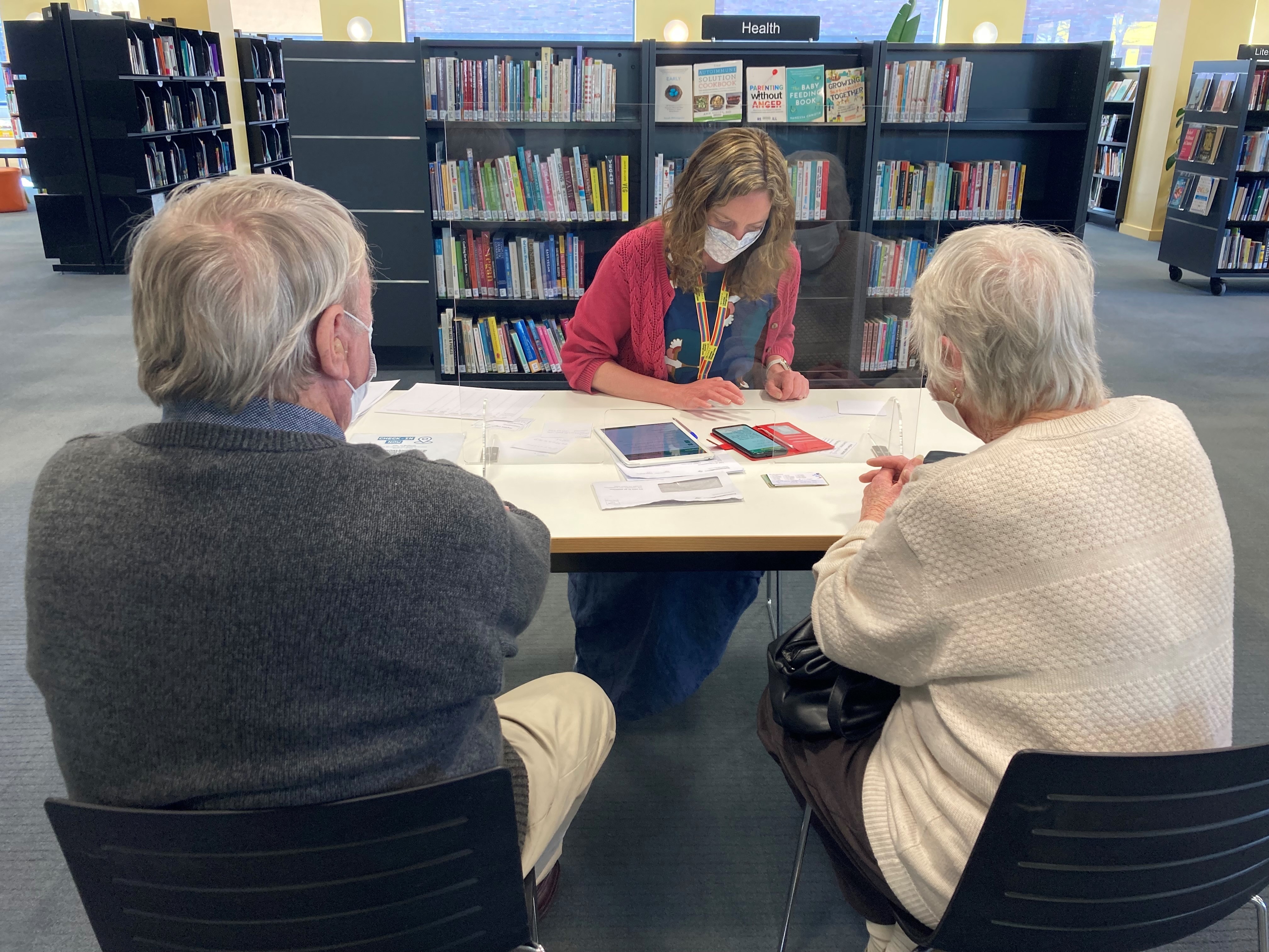A woman with an iphone and papers on a table with two people sitting across from her.