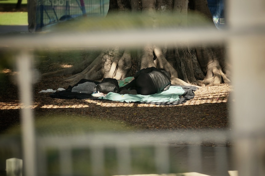 A homeless person sleeps on a blanket in a Brisbane park