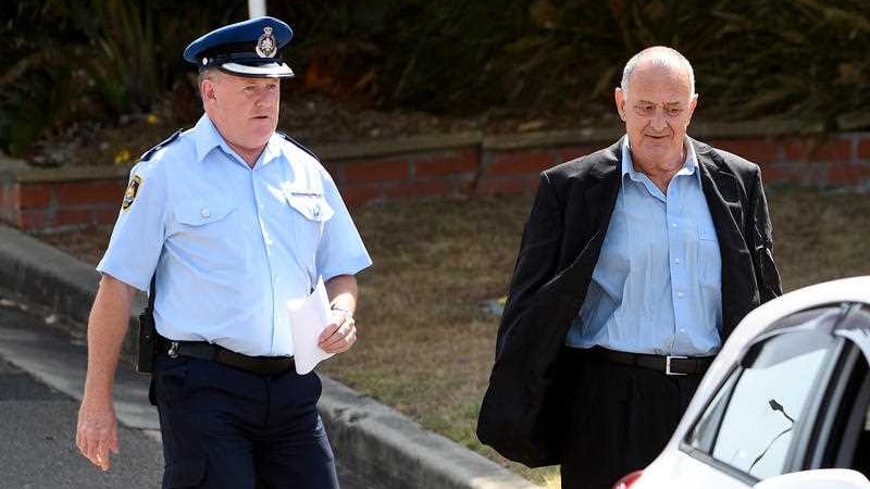 A man in a suit walking away from a prison accompanied by a policeman.