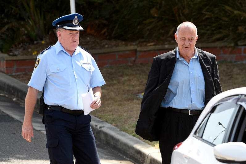 A man in a suit walking away from a prison accompanied by a policeman.