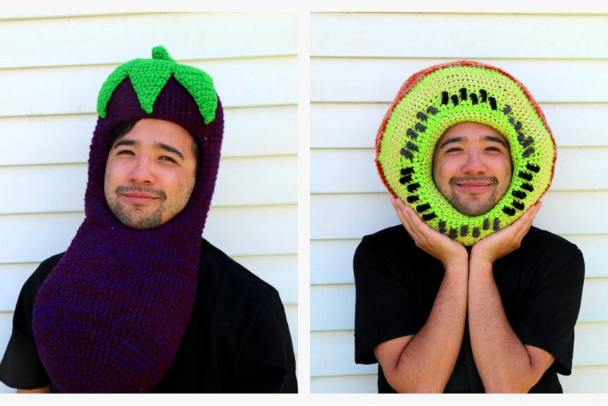 A young man in a crocheted eggplant hat and crocheted kiwi hat.