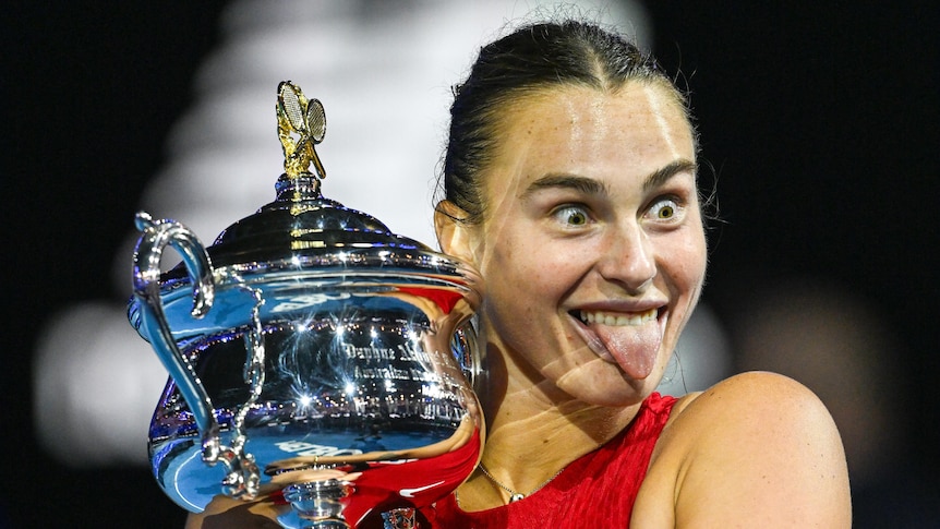 Aryna Sabalenka sticks her tongue out while holding the Daphne Akhurst Memorial Cup after winning the Australian Open.