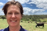 Female farmer, with cows in paddocks behind her.