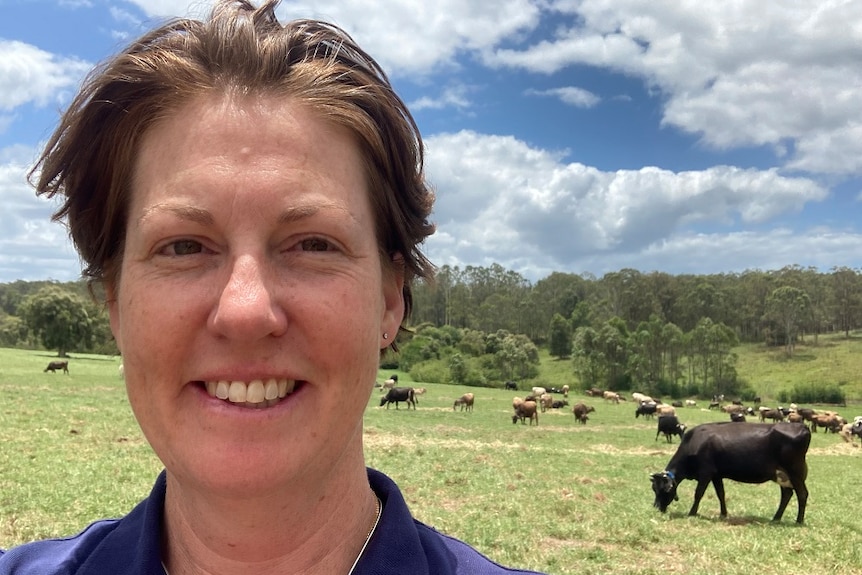 Female farmer, with cows in paddocks behind her.