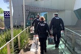 Three police walking into a station carrying seized weapons
