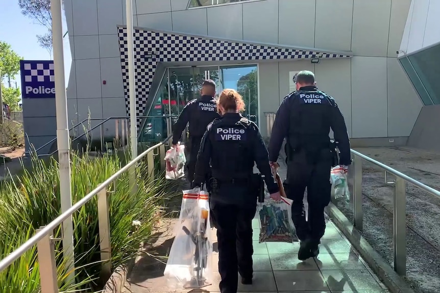 Three police walking into a station carrying seized weapons