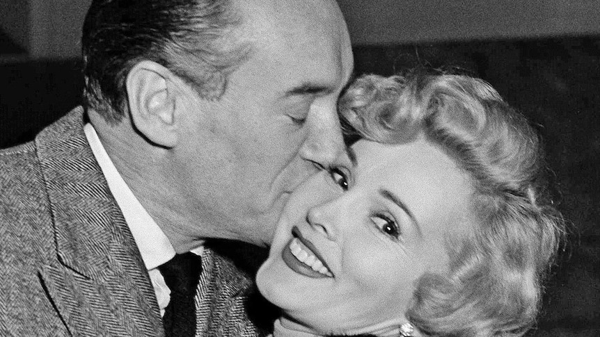 George Sanders kisses Zsa Zsa Gabor in a black and white photograph from the 50s.
