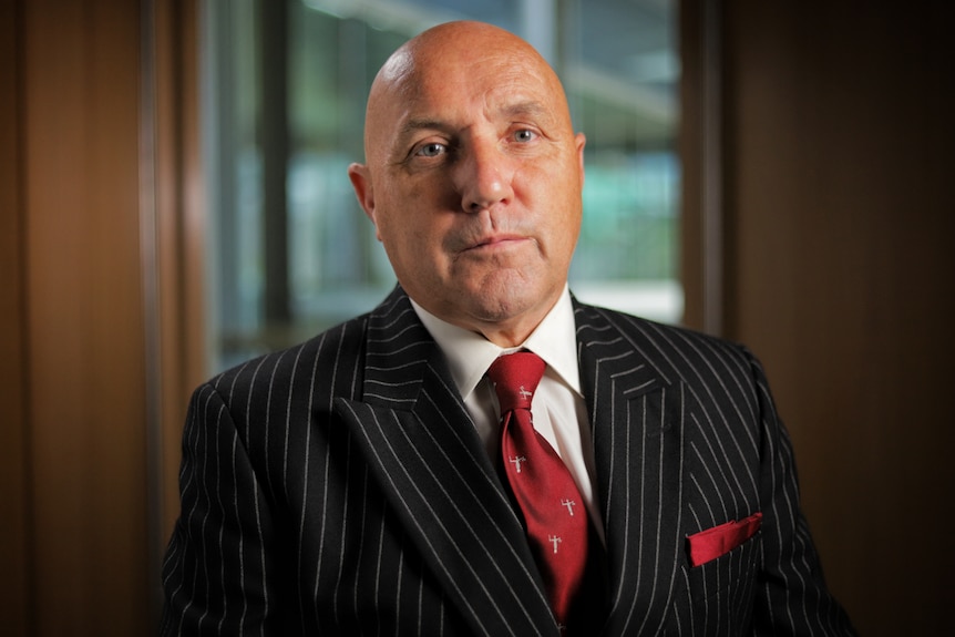 A man wearing a black pinstripe suit and a red tie.