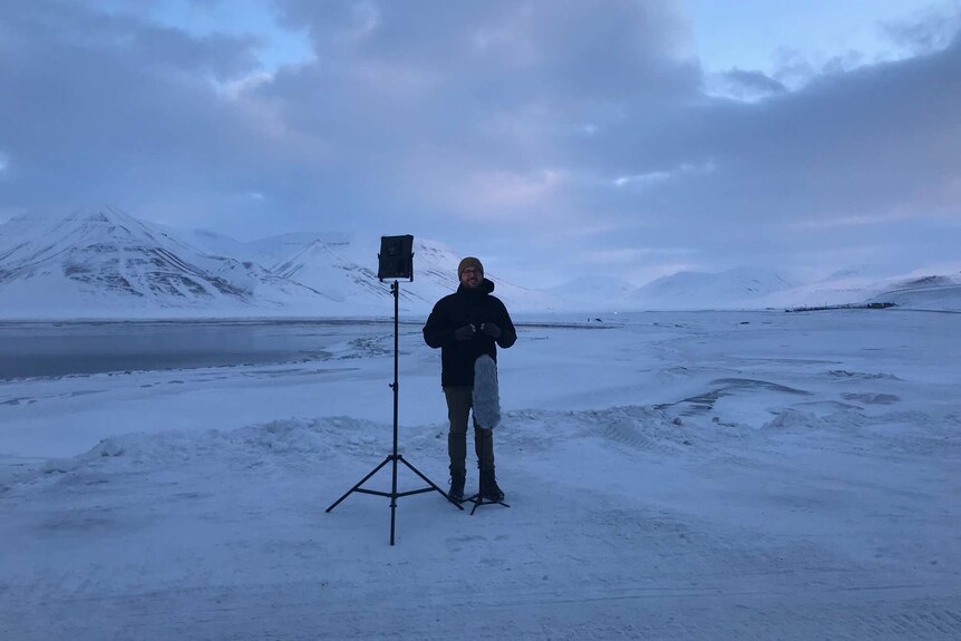 Steven Schubert standing in front of microphone next to light in snow-covered landscape.