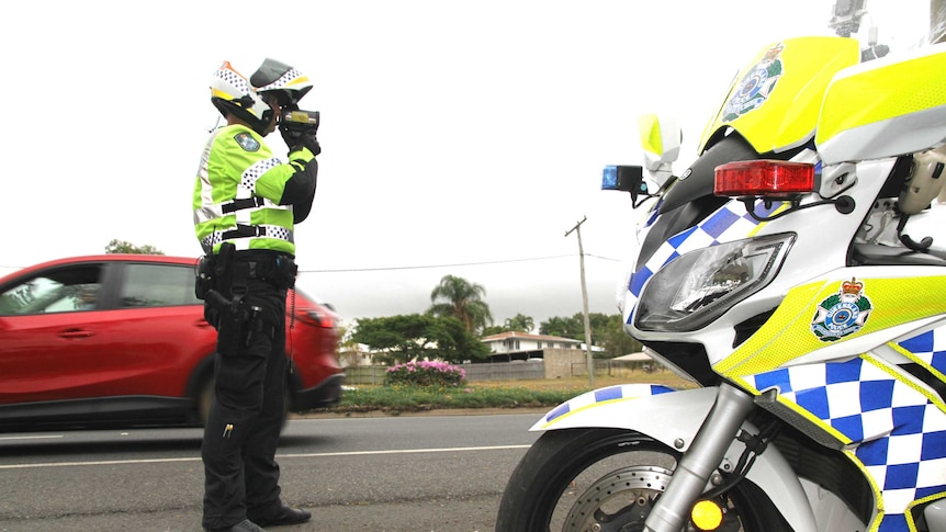 A police officer stands beside his motorcycle on a busy road.