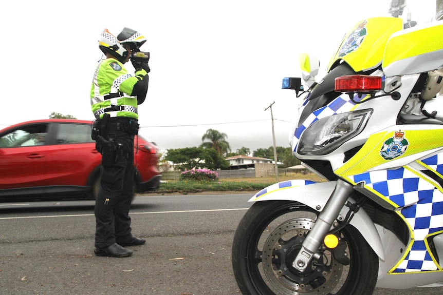 A police officer stands beside his motorcycle on a busy road.