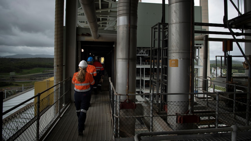 Workers move through a door at the top of a power plant, with a view below