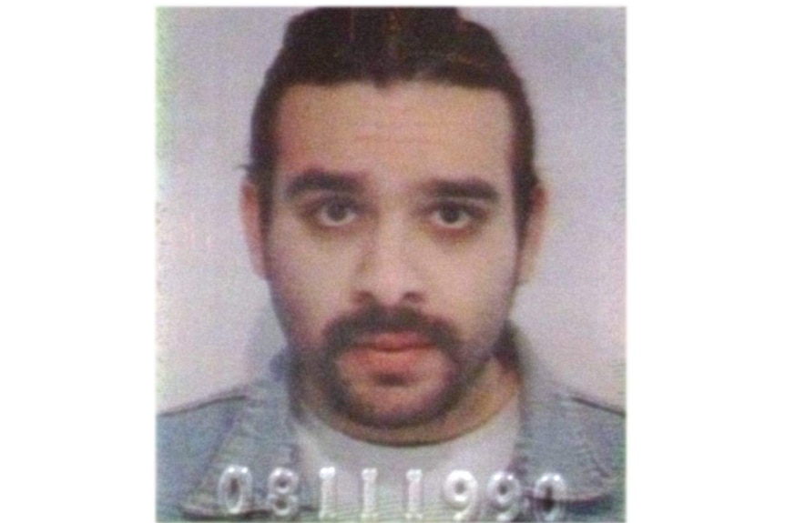 A mugshot of a man with long black hair and a goatee wearing a blue shirt.