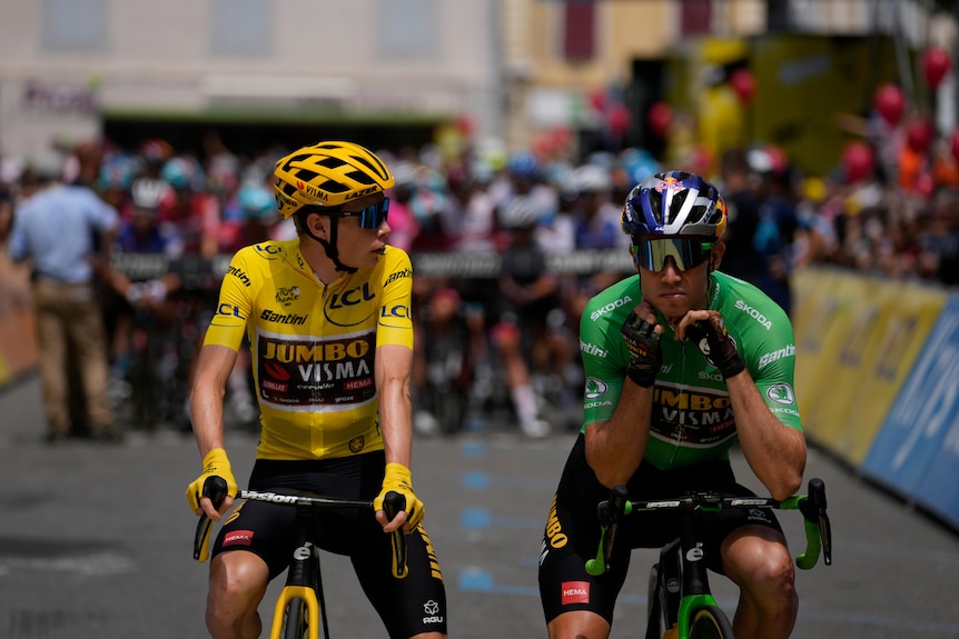 The yellow jersey rider and green jersey rider sit on their bikes talking before a Tour de France stage. 