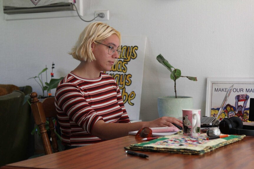A woman with cropped blonde hair sits in front of her laptop.