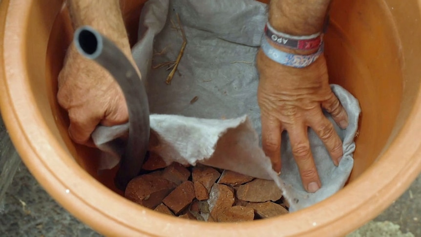 Geotextile fabric being put on top of crushed rocks inside a plastic pot.