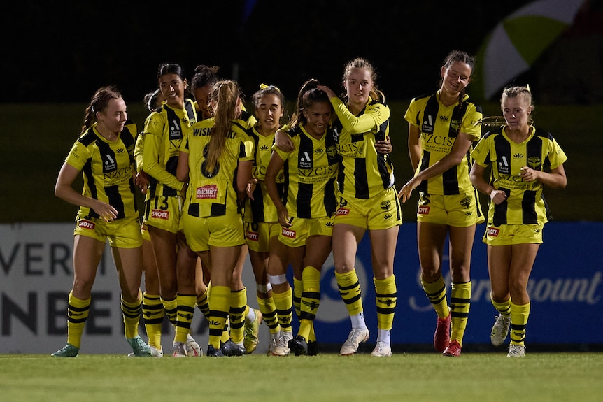 Soccer players wearing yellow and black stripes celebrate after scoring a goal