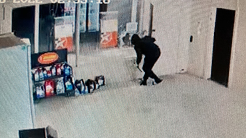 A person in a black tracksuit at the front window of a service station. 
