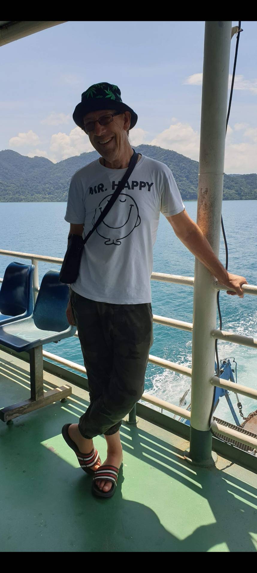 A happy-looking male of pension age in a bucket hat and white tee on a boat in tropical surrounds.