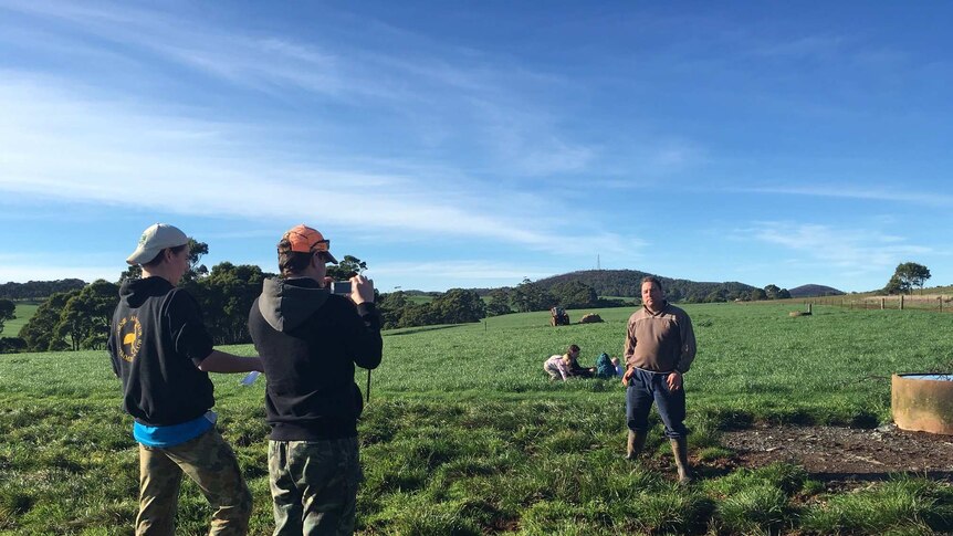 two boys in paddock filming a dairy farmer