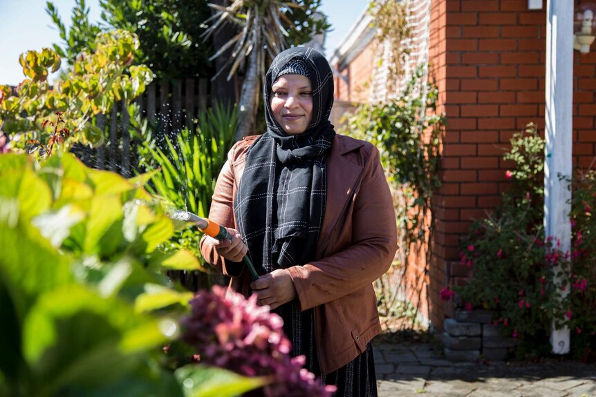 A woman in a headscarf waters the garden
