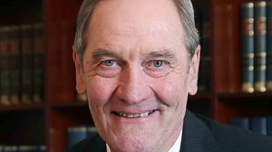 A headshot of an older Caucasian man with green eyes and light silver brown hear smiling at the camera in a suit and tie.