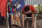 A woman and a man sit on plastic chairs and cry.