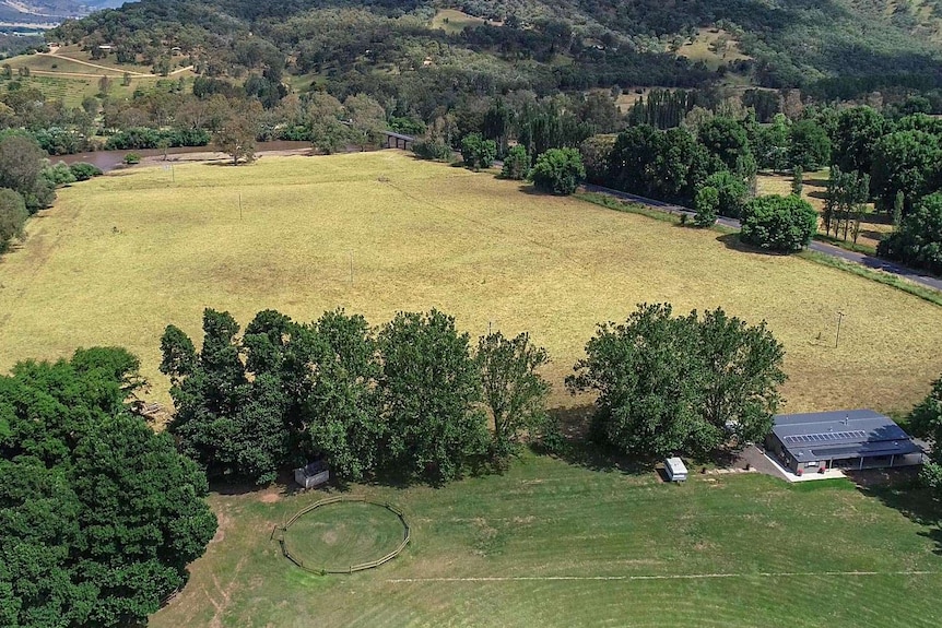 A drone shot of a football oval, behind is a paddock and the Murray River, with a bridge crossing over and rolling hills behind.