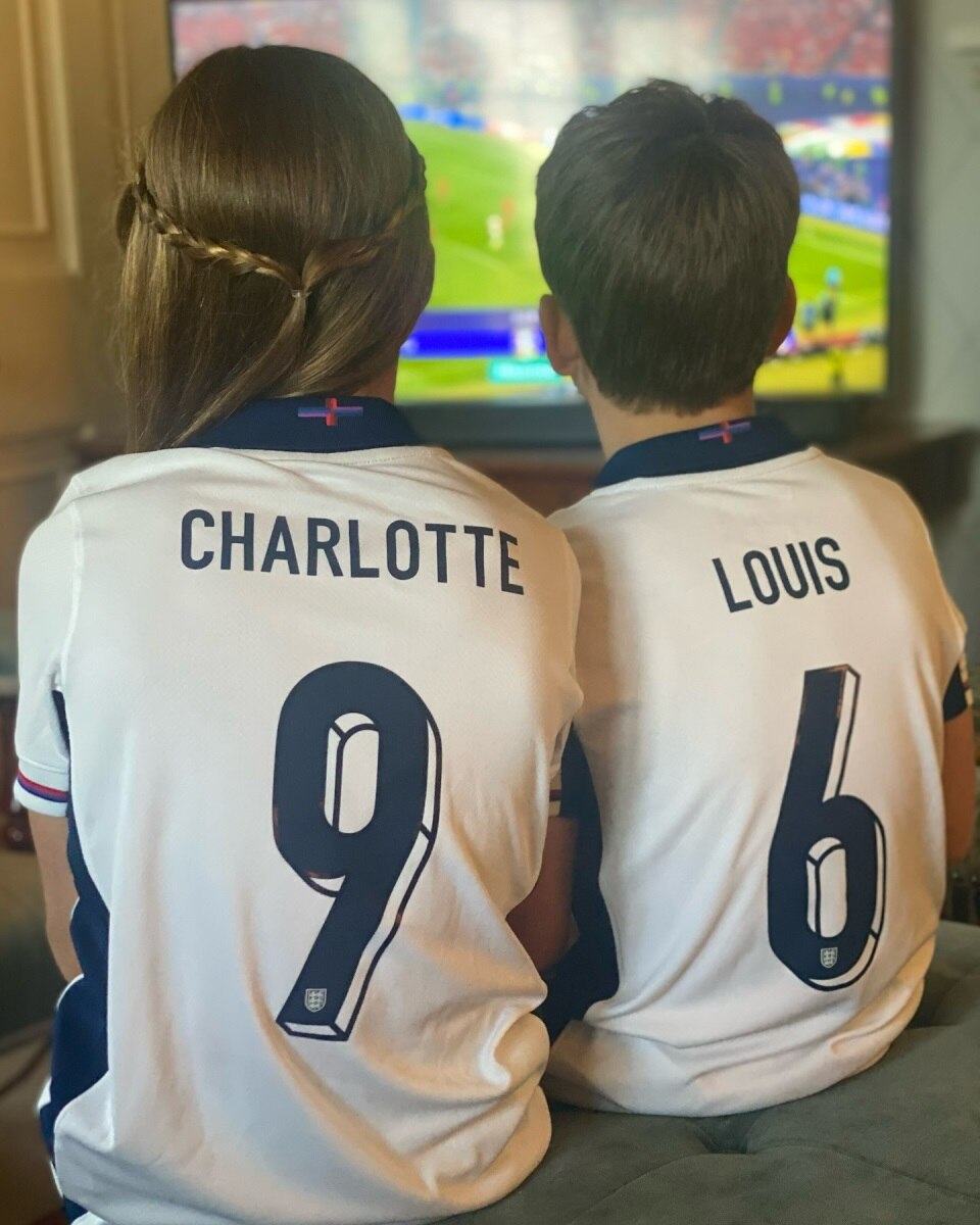 Charlotte and Louis sit side-by-side watching football ont eh TV, wearing jerseys emblazoned with their names.