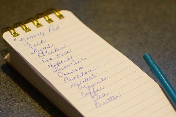 A pen on a notepad with a list of grocery items including milk, eggs and apples.