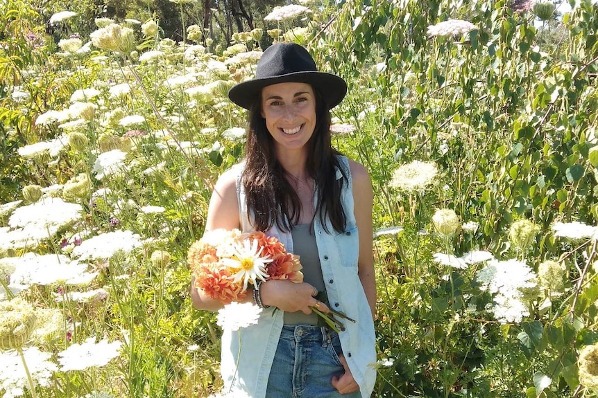 woman smiling, looking relaxed, holding flowers, in a field of slowers 